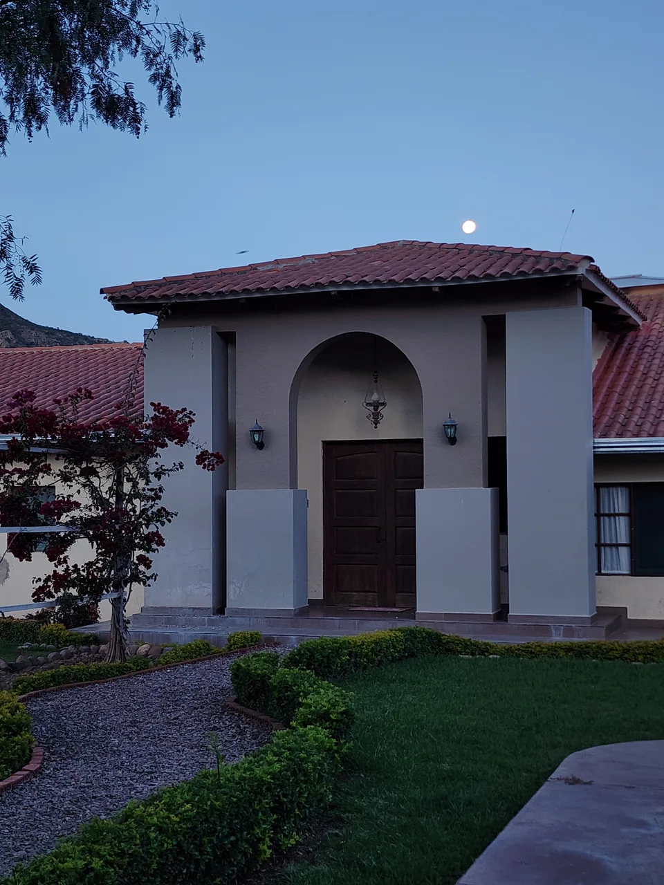 Entrada principal de la villa al atardecer con la luna sobre el tejado