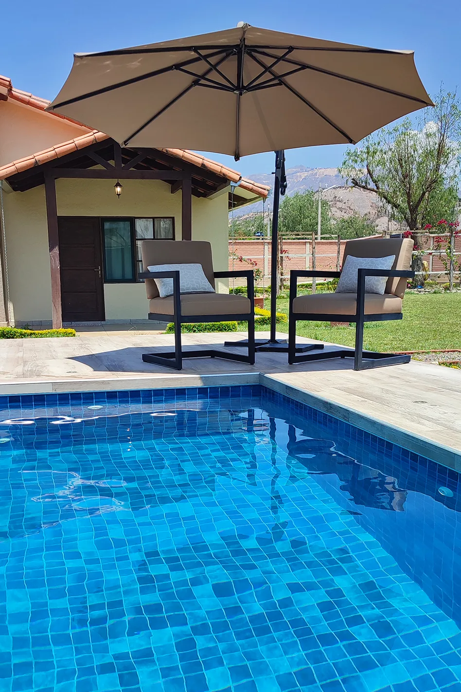 Piscina y sillones bajo una sombrilla junto al jardín